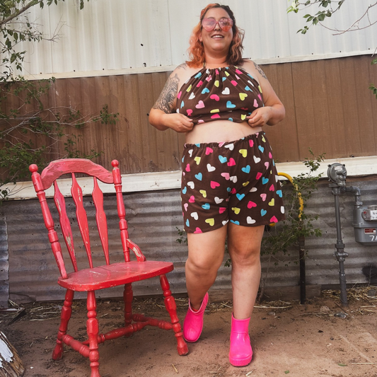 Person wearing a patterned outfit with pink shoes standing next to a red chair outdoors.
