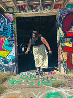 Woman wearing Happy Daze Upcycled Bedsheet Skirt with smiley faces, standing in a graffiti-covered doorway.