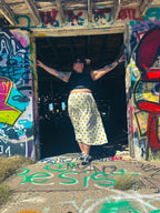 Woman wearing a Happy Daze Upcycled Bedsheet Skirt with smiley faces in a vibrant, graffiti-filled setting.