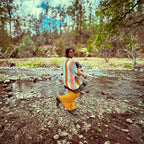 A woman wearing 🛸 Golden Mirage Flare Pants – One of a Kind Upcycled Statement Piece, walking by a stream surrounded by nature.