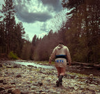 Person walking by a river wearing YETI hoodie in nature, showcasing colorful outdoor fashion.