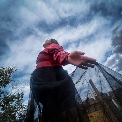 Woman showcasing the Betty in Paris Reworked Hoodie Dress with flowing black sheer skirt against a cloudy sky.
