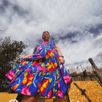 A woman in a colorful floral Bloom Riot Maxi Dress, showcasing unique women's clothing with a vibrant design.